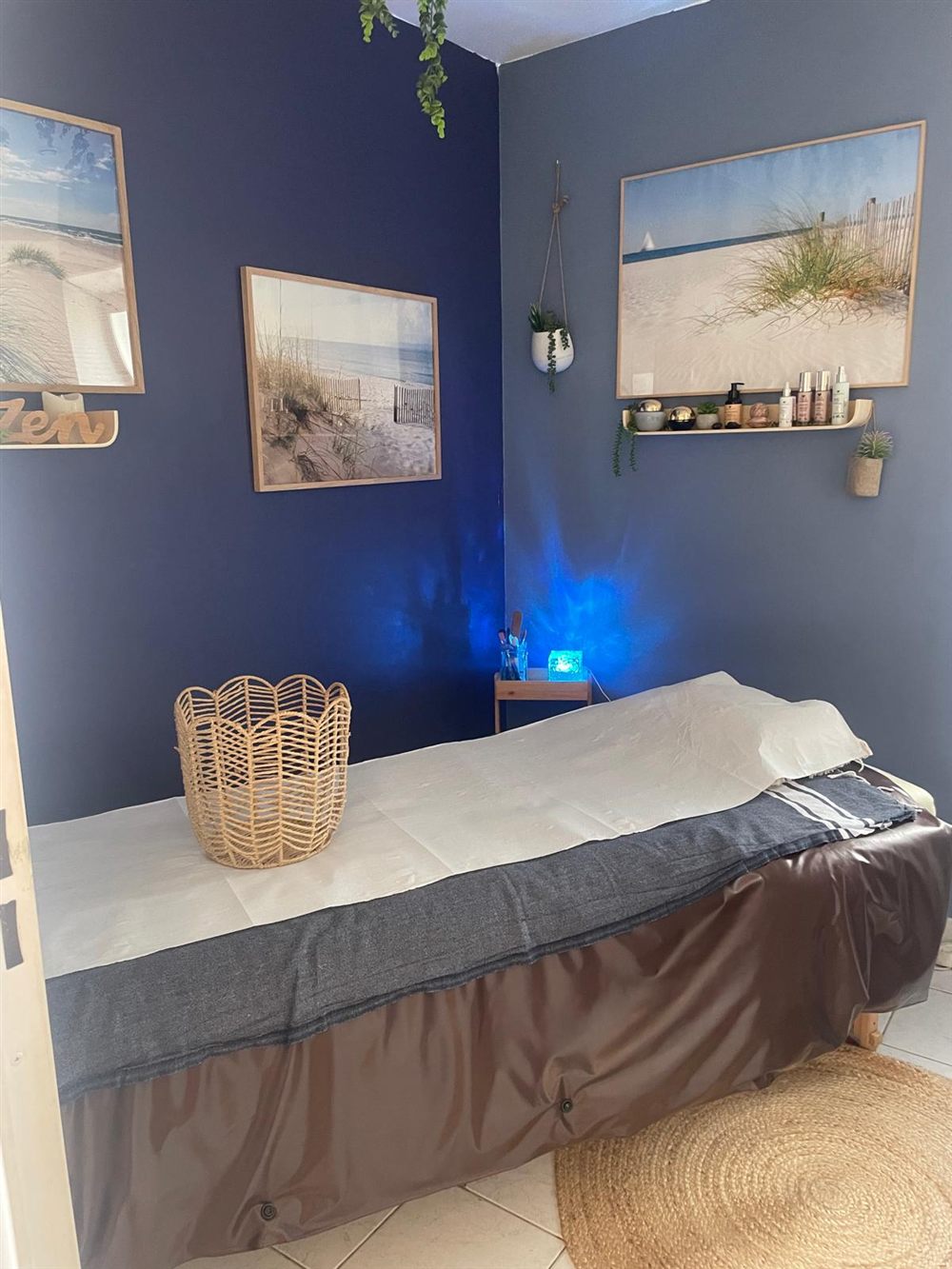 La cabine de soin : murs bleu nuit, tableaux de dunes, table de soin et tapis en jute